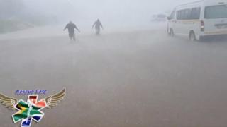 People wade through flood water in strong winds and rain next to submerged vehicles on a road during stormy weather in Durban, South Africa , 10 October 2017