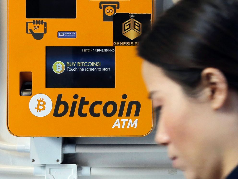 FILE - In this Dec. 21, 2017 file photo, a woman walks past the Bitcoin ATM in Hong Kong.