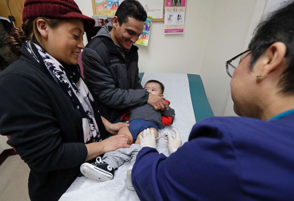 PHOTO: Matilde Gonzalez, left, and Cesar Calles, hold their son, Cesar Julian Calles, 10-months old, as Ana Martinez, a medical assistant at the Sea Mar Community Health Center, gives him a flu shot, Jan. 11, 2018, in Seattle. 
