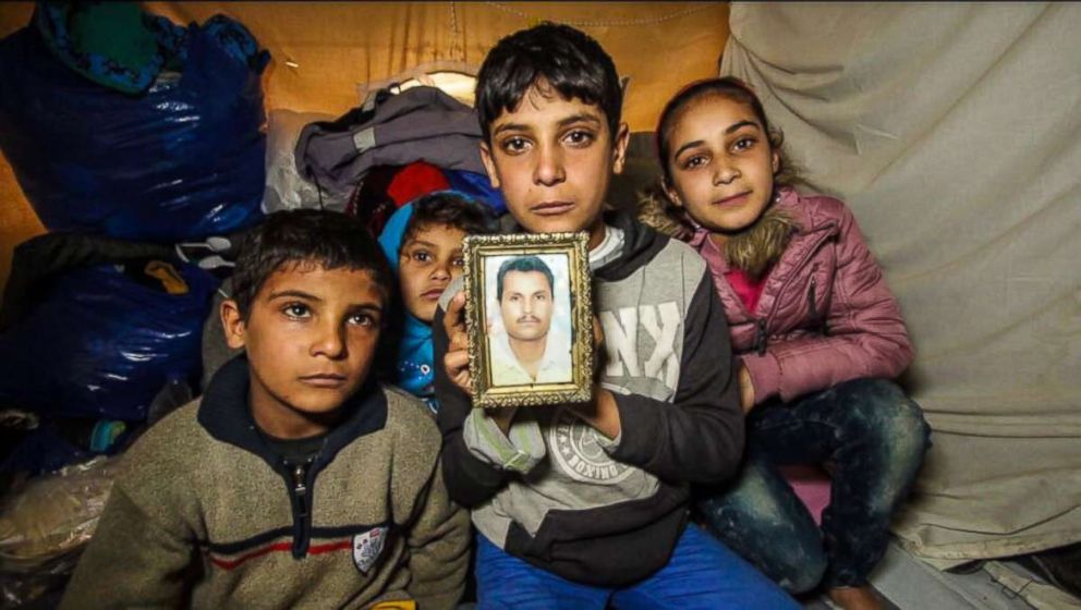 PHOTO: Anas Hommada, 14, sits in his tent in Lesbos Moria camp with three of his siblings holding a photo of his missing father, Amer.