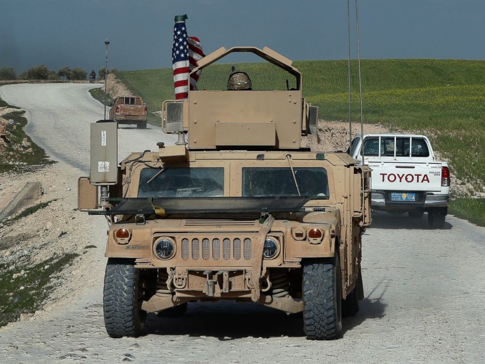 In this picture taken on Thursday, March 29, 2018, U.S. troops humvee passes vehicles of fighters from the U.S-backed Syrian Manbij Military Council on a road leading to the tense front line with Turkish-backed fighters, north of Manbij town, Syria.